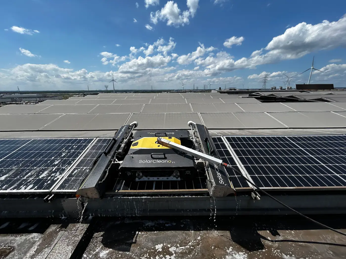 Robot de nettoyage sur un toit industriel plat, avec des éoliennes en arrière-plan